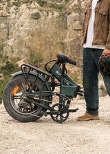 a man stands next to a folded sea green engwe engine pro 2.0 e-bike